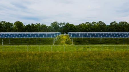 pexels-photo-4320481-4320481 Aerial view of solar panels in a grassy field with trees in the background.